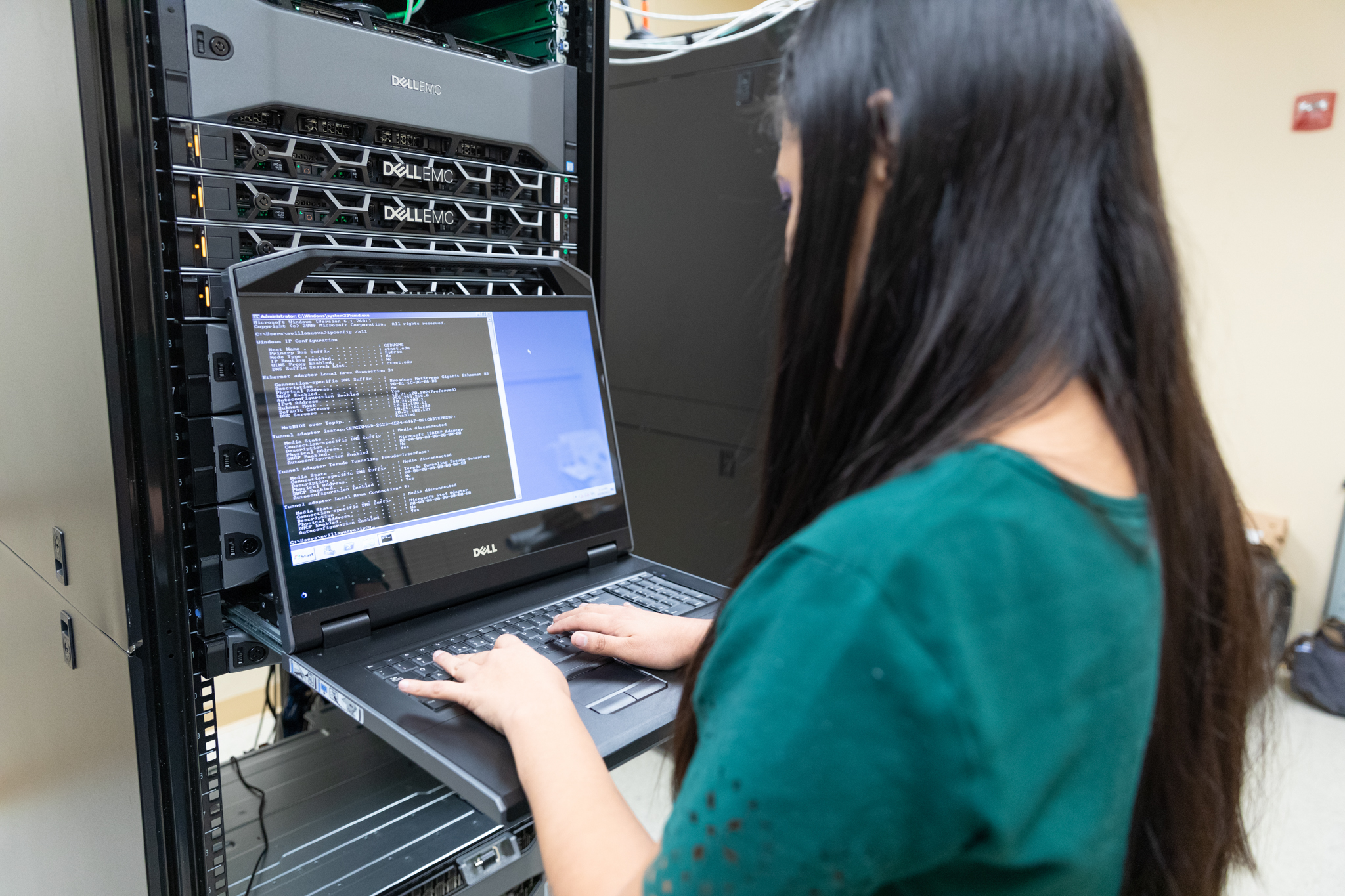 woman with long straight hair and a green blouse stands in front of a computer typing