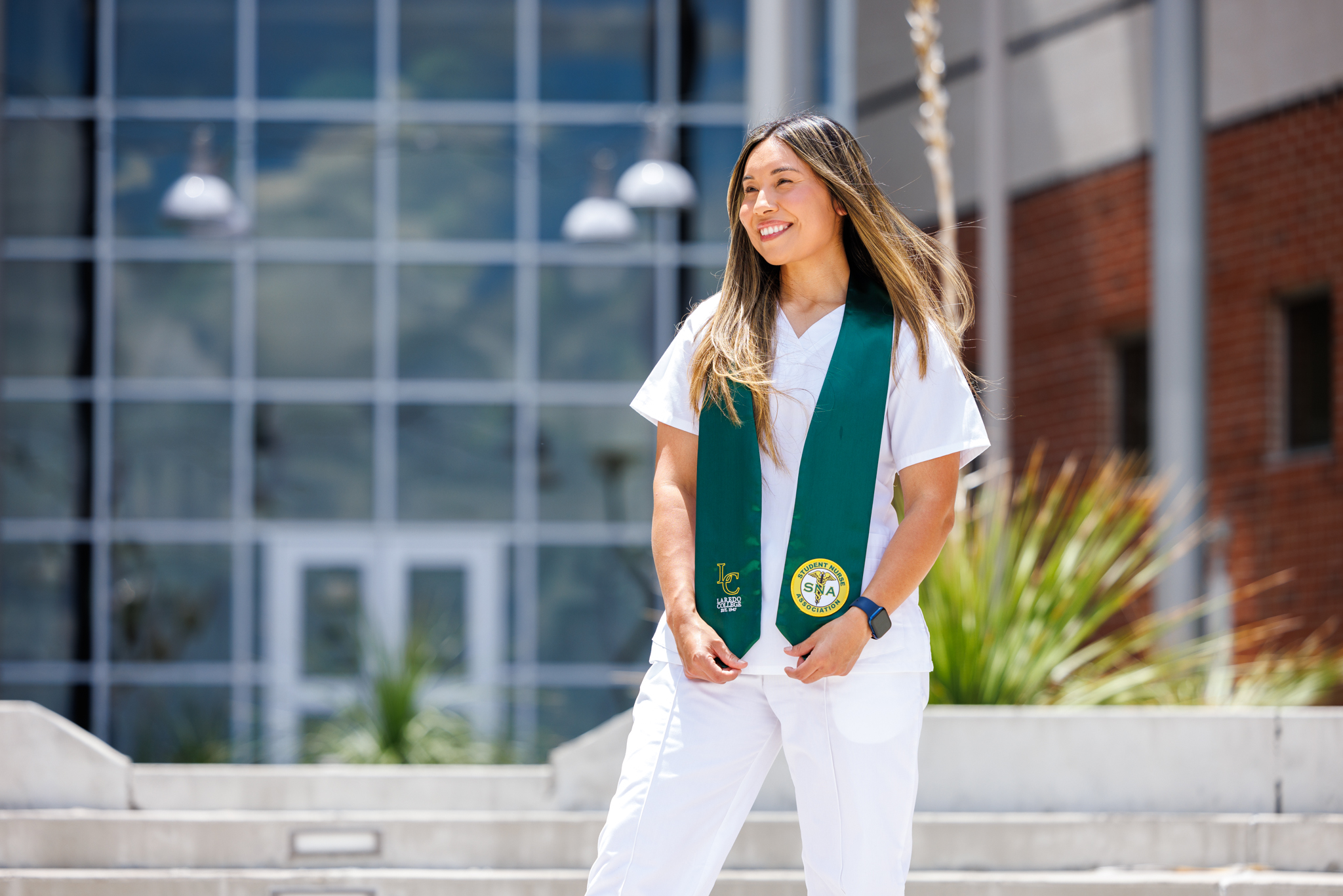 Associate Degree of Nursing student standing outside the College of Health Sciences in her white scrubs and green stole.